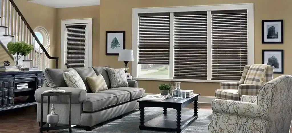 Living room with gray sofa, patterned chair, wooden blinds, and artwork on the wall.