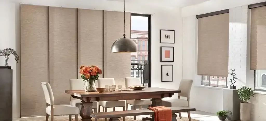 Dining room with a large wood table, upholstered chairs, and roller shades
