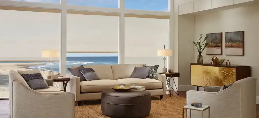 Oceanfront living room with beige furniture and white roller shades on floor-to-ceiling windows