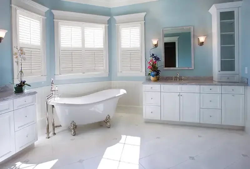 Elegant blue and white bathroom with a clawfoot tub, vanity, and large windows.