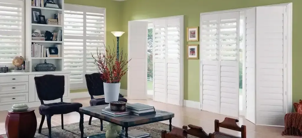 Living room with white shutters, green walls, furniture, and a coffee table with decor.