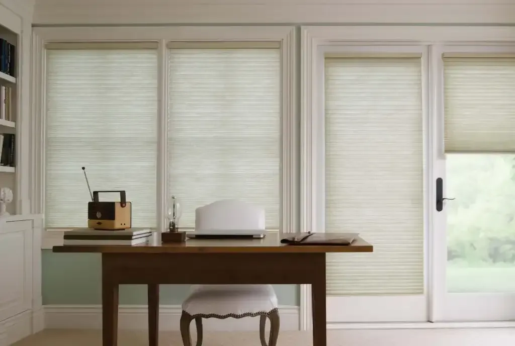 Home office desk facing three windows and a door with light cellular shades