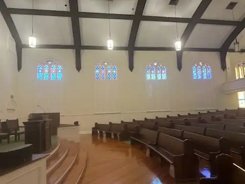 Church sanctuary with a row of arched stained glass windows and custom white shutters above wooden pews
