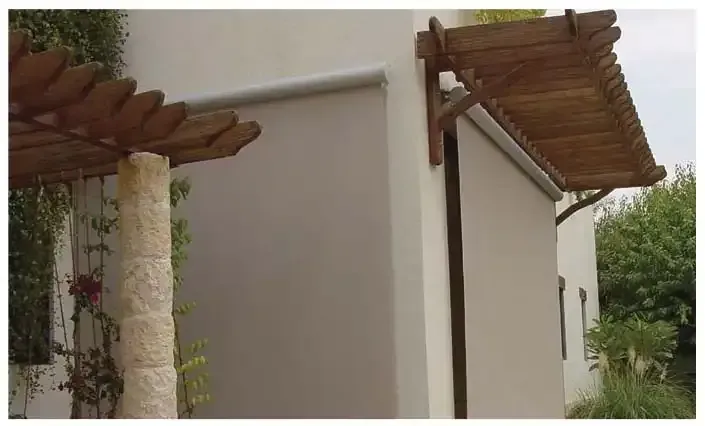 Exterior wall with a wooden pergola and a lowered tan outdoor solar shade