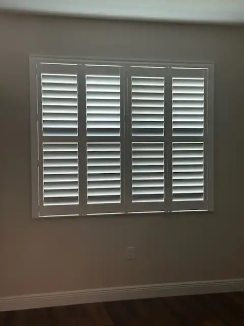 Four-panel white plantation shutters with divider rails covering a wide window