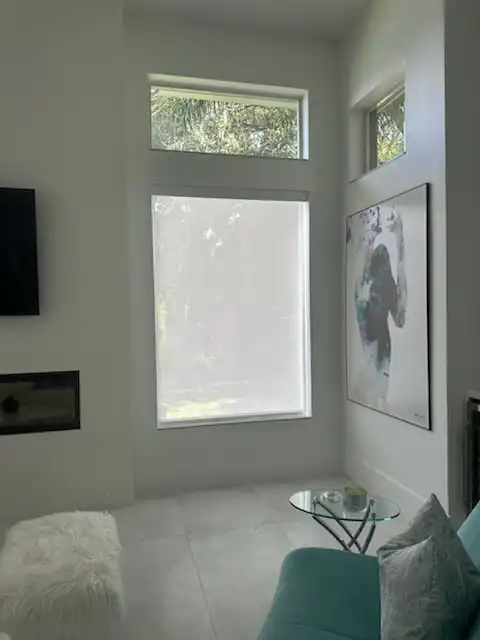 Light filtering roller shade fully lowered on a tall living room window below a transom window