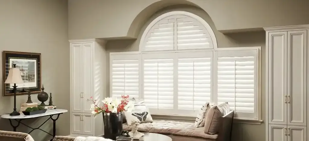 Window seat under an arched window fitted with plantation shutters