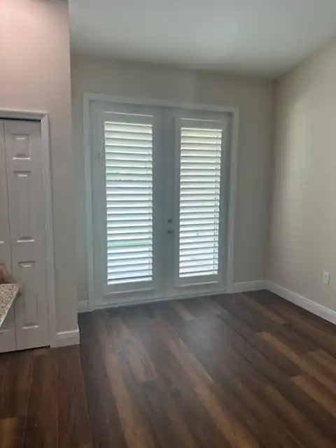 White plantation shutters mounted on a pair of French doors in a room with dark wood floors