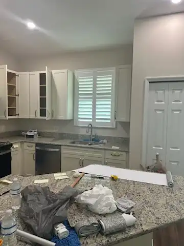 White plantation shutters on a kitchen window above the sink, between white cabinets