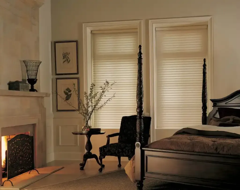 Bedroom with a fireplace, dark four-poster bed, and sheer shadings on two windows