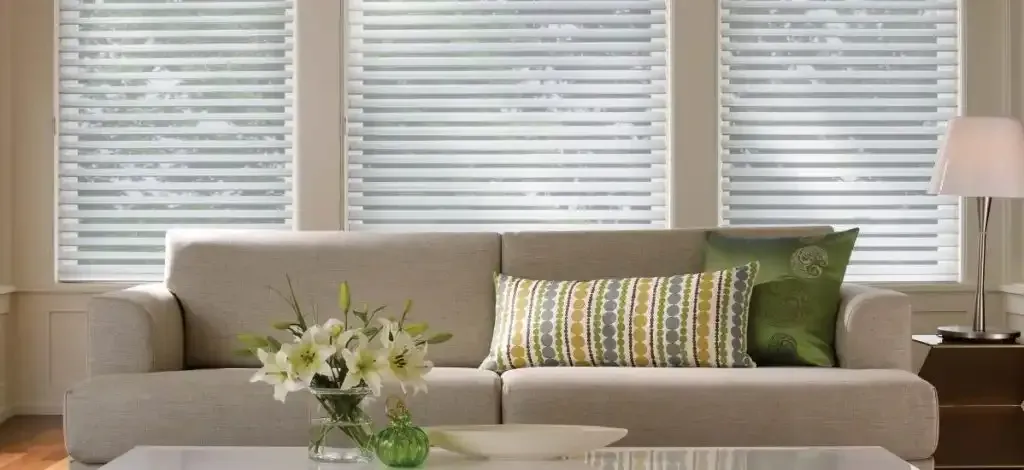 Living room with a tan sofa and white sheer shadings on three windows