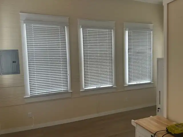 Row of three windows with white horizontal blinds and painted trim