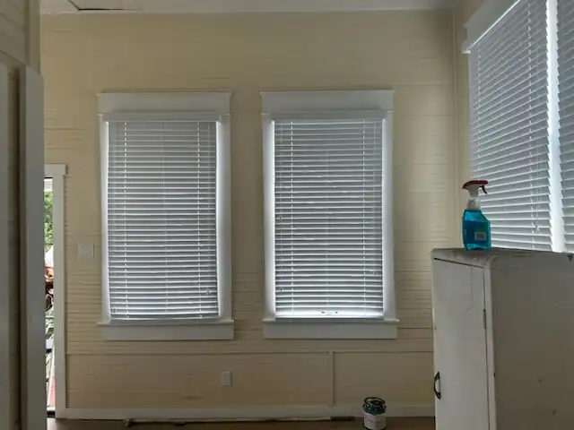Two cottage windows with newly installed white horizontal blinds and wide painted trim