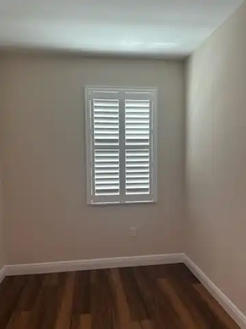 White plantation shutters with louvers tilted open on a single window in a small bedroom with dark wood floors