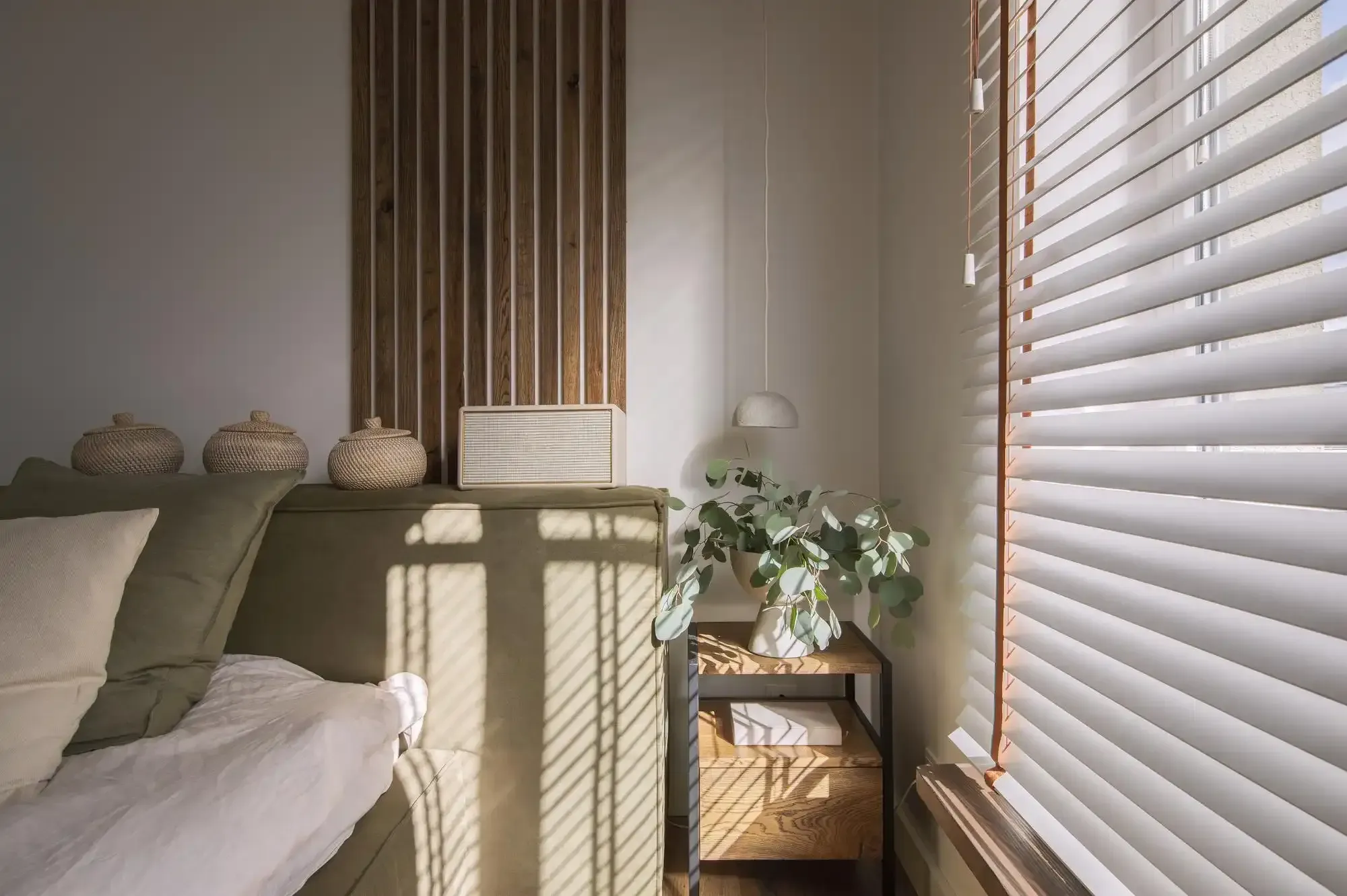 Sunlit bedroom corner with white wood blinds on two windows
