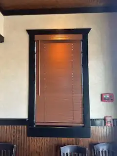 Stained wood blinds lowered on a restaurant window framed with dark trim